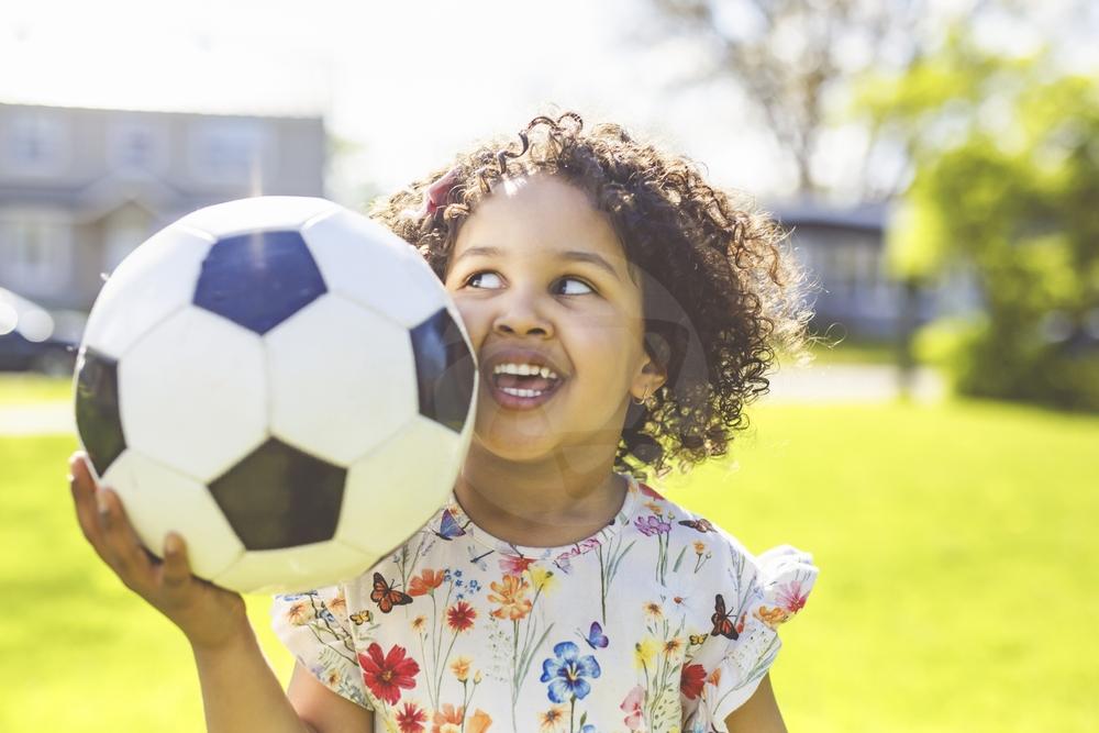 Menina negra segura bola de futebol e sorri